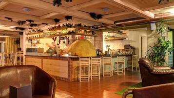 A bar area with wooden chairs, a counter with bottles, and a kitchen in the background.