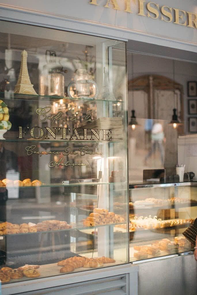 Une devanture de magasin avec une vitrine remplie de pâtisseries et une enseigne indiquant « Café de la FONTAINE ».