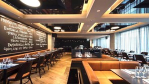 A restaurant with a long counter, multiple tables, and a blackboard menu.