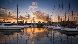 A marina with multiple sailboats docked, reflecting the sunset in the calm water.