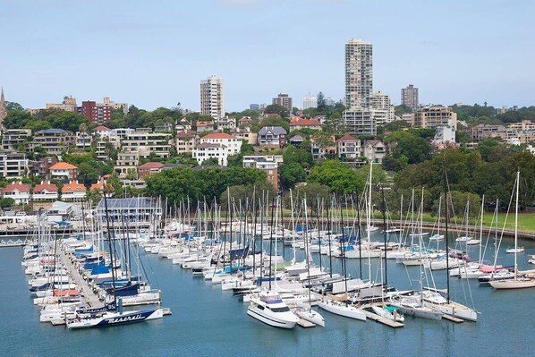 Un port de plaisance où sont amarrés de nombreux voiliers, entouré d’immeubles résidentiels et de verdure.