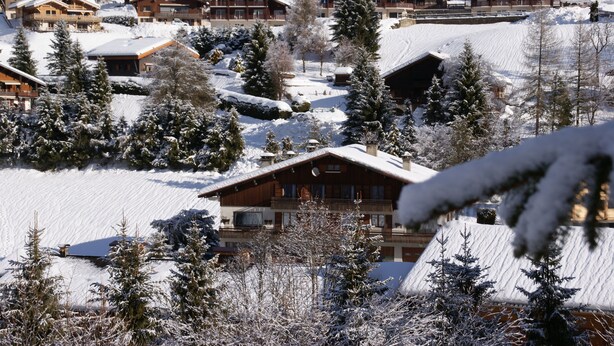 A snow-covered lodge with multiple wooden buildings, surrounded by snow-laden trees and a ski slope. - Large, cosy apartment in exceptional location near village. (La Clusaz)