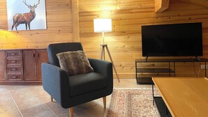 A cozy living room with a wooden interior, a comfortable armchair, a flat-screen TV, and a painting of a deer on the wall. - Large, cosy apartment in exceptional location near village. (La Clusaz)