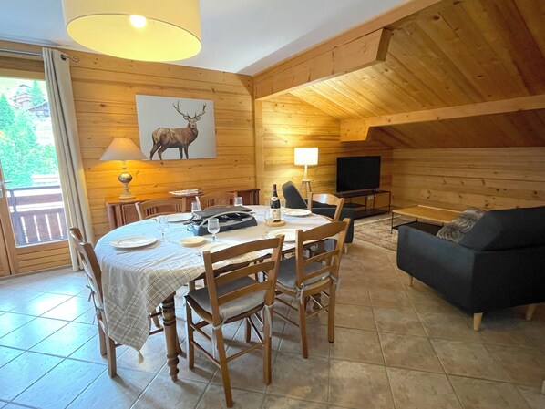 Une chaleureuse cabane en bois dotée d’un coin repas avec une table dressée pour quatre personnes, d’un canapé et d’un téléviseur placé dans un coin.