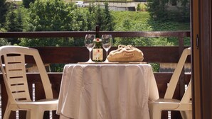 A balcony with a table set for two, overlooking a mountainous village with houses and greenery. - Large, cosy apartment in exceptional location near village. (La Clusaz)