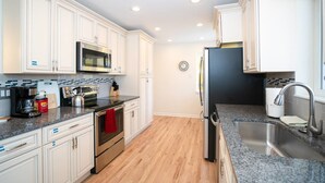 A modern kitchen with white cabinetry, stainless steel appliances, a granite countertop, and a wooden floor. - The Meadowlark Manor Spacious Backyard & Hot Tub (Lakewood)