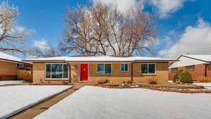 A two-story brick house with a red door, large windows, and a snow-covered driveway. - The Meadowlark Manor Spacious Backyard & Hot Tub (Lakewood)