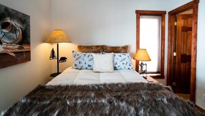 Une chambre à coucher avec un grand lit, deux lampes de chevet, une porte en bois et une œuvre d’art accrochée au mur.