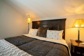 A neatly made bed with a dark quilt, two bedside lamps, and a wooden headboard. - The Mountain Escape in Vail (Vail)