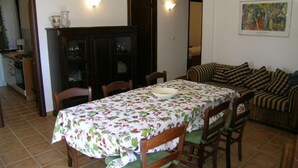 Een eetruimte met een tafel voor vier personen, omringd door stoelen. Er staat een kast met glazen en er hangt een schilderij aan de muur.