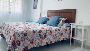 A bedroom with a floral bedspread, a wooden headboard, a bedside table with a lamp, and a wall-mounted mirror. - BEAUTIFUL APARTMENT IN PORTOSIN (porto do son)