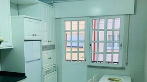 A kitchen with white cabinets, a stove, a refrigerator, a window with bars, and a table with chairs. - BEAUTIFUL APARTMENT IN PORTOSIN (porto do son)