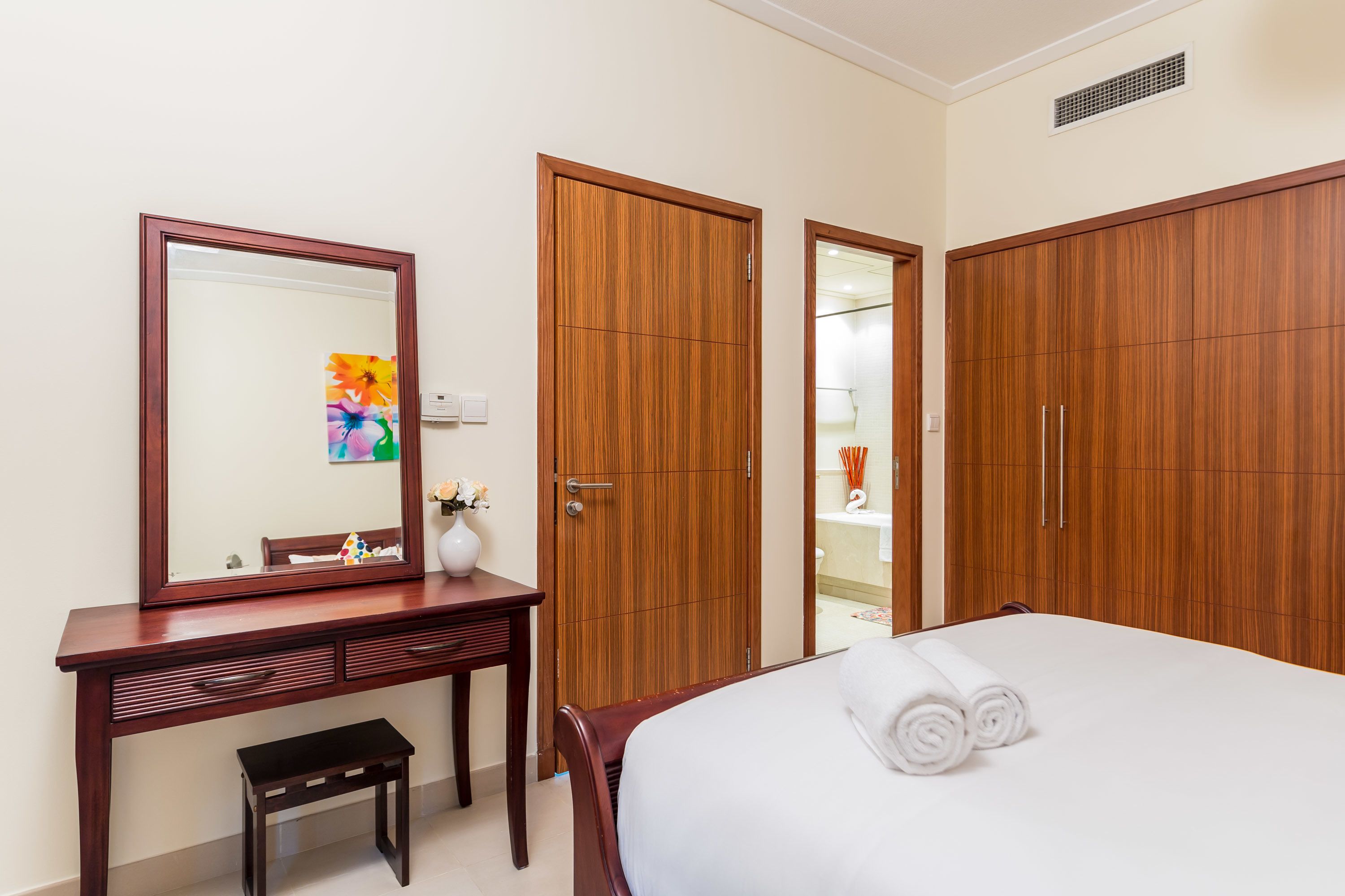 Una camera d'hotel con un letto, un armadio in legno, uno specchio e un tavolino con un vaso.