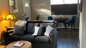 Un salon comprenant un canapé, une table basse, une lampe, un ventilateur de plafond, une table à manger avec des chaises et une grande fenêtre.