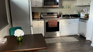 Une cuisine moderne avec des meubles blancs, des appareils en acier inoxydable et une table à manger en bois, assortie de chaises de couleur turquoise.
