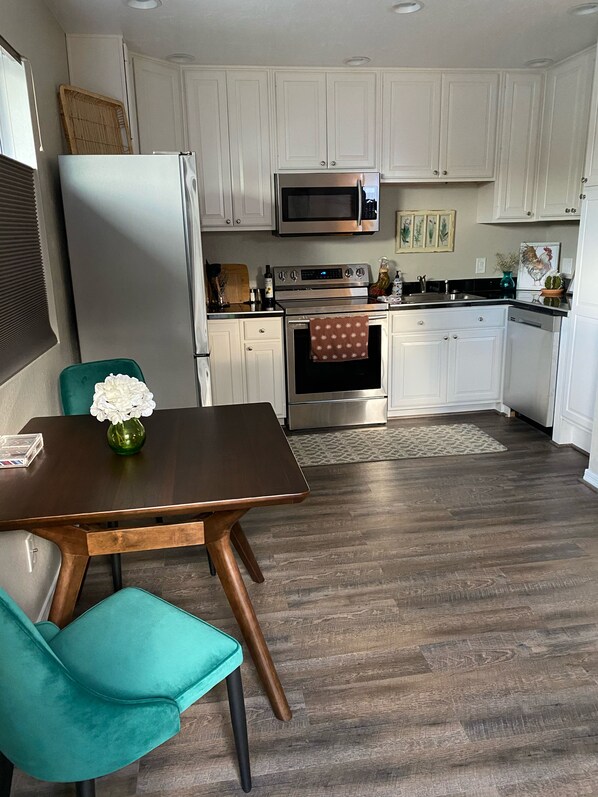 A modern kitchen with white cabinets, stainless steel appliances, and a wooden dining table with teal chairs. - CONVENIENTLY LOCATED ONE BEDROOM APARTMENT IN NORTH PHOENIX (Phoenix)
