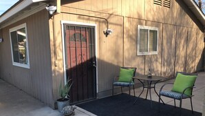 Une maison en bois avec une porte rouge, deux chaises avec des coussins verts et une petite table.
