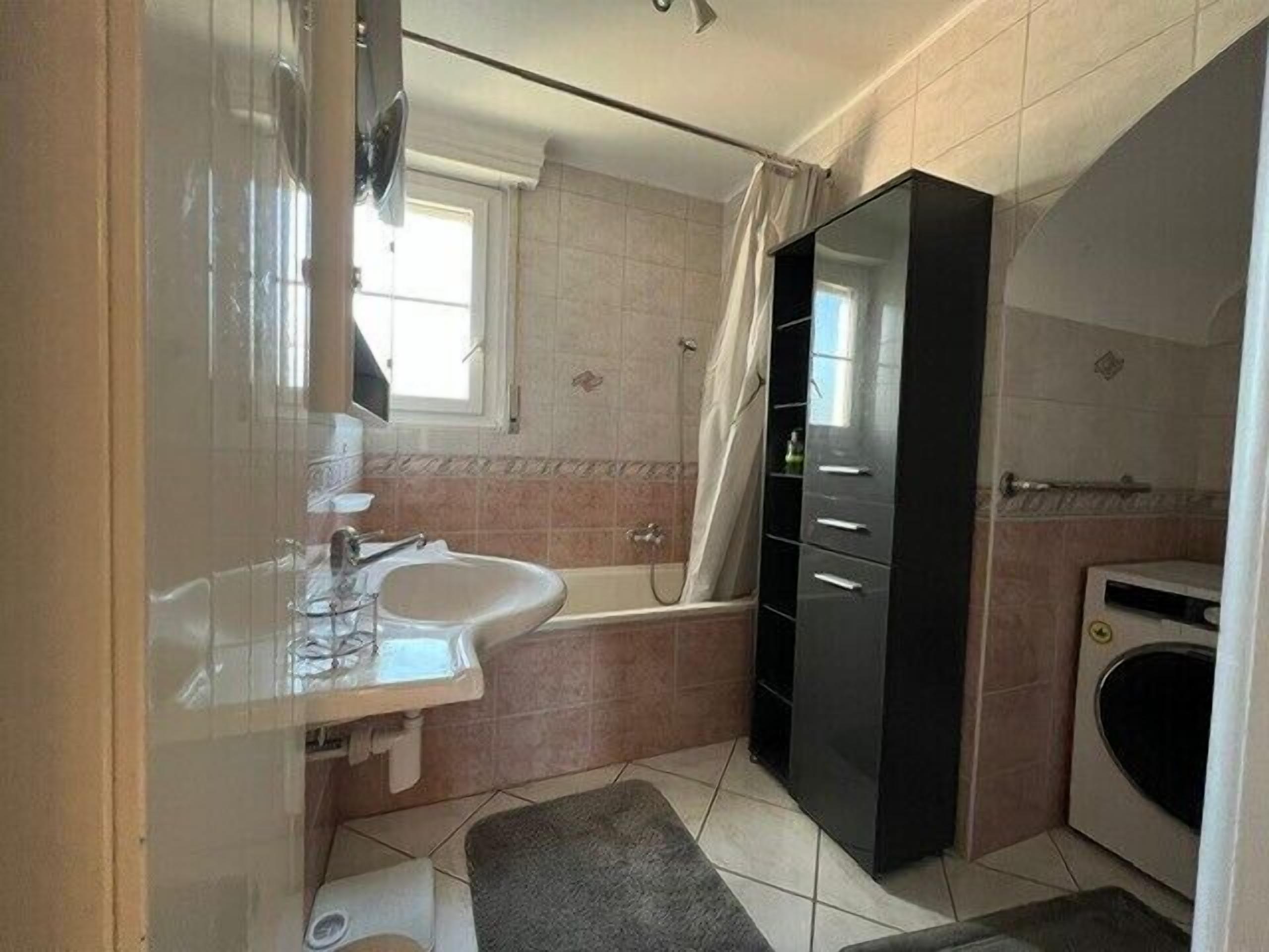 Een badkamer met een wastafel, spiegel, badkuip en een wasmachine.