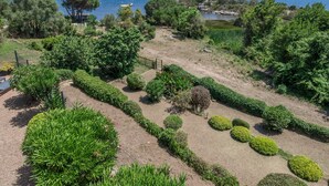 Ein gepflegter Garten mit ordentlich geschnittenen Hecken und verschiedenen Sträuchern, der zu einem Gewässer mit Booten führt.