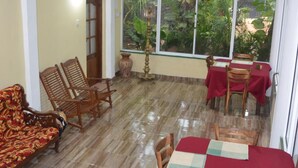 A dining area with a table set for four, surrounded by wooden chairs. There is a ceiling fan above and a window with a view of greenery outside. - Green Garden Resort (Habarana)