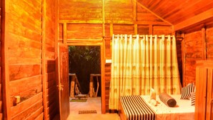 A wooden cabin interior with a bed, curtains, and a door leading outside. - Green Garden Resort (Habarana)