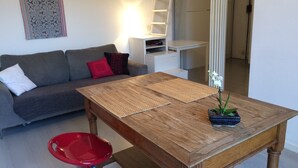 A modern living room with a wooden coffee table, a red chair, a grey sofa with red and black cushions, and a small potted orchid.