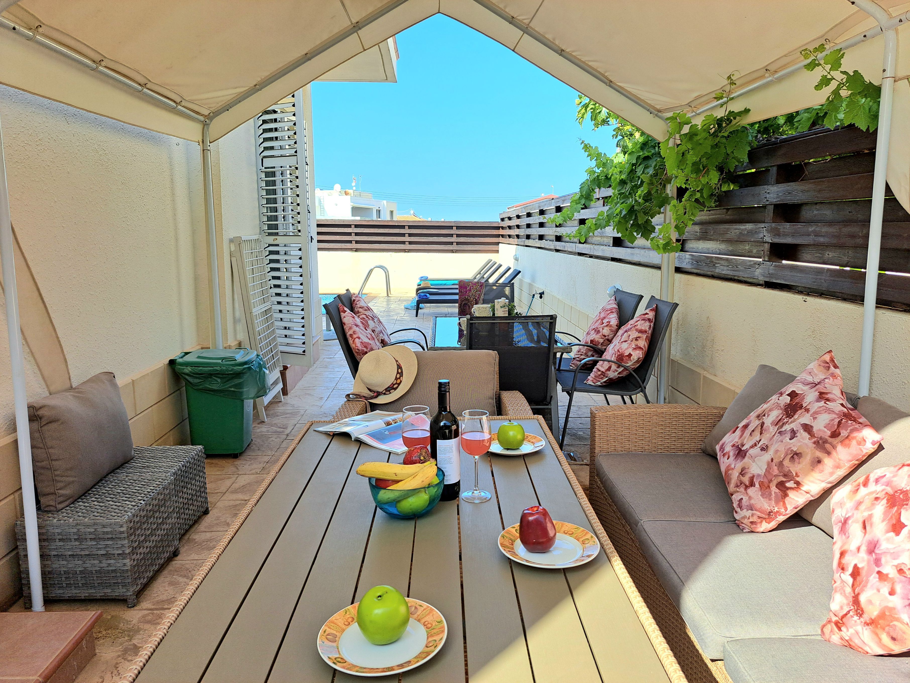 An outdoor patio with a table set for dining, a sofa, and a chair.