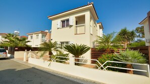 A two-story residential building with a balcony, surrounded by palm trees and a gated entrance. - Villa Anasta near the sea  (Protaras)