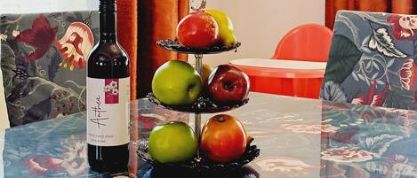 A table with a bottle of wine, a fruit stand, and a floral tablecloth.