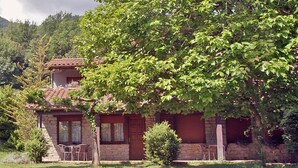 A stone house with a tiled roof, surrounded by lush greenery and trees. - Allotjaments Colomer-Cullell (La Vall d'en Bas)