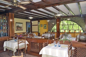 A restaurant with wooden furniture, white tablecloths, and a stone wall. - Allotjaments Colomer-Cullell (La Vall d'en Bas)
