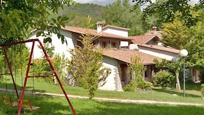 A house with a red swing set in the foreground, surrounded by a well-maintained lawn and trees. - Allotjaments Colomer-Cullell (La Vall d'en Bas)