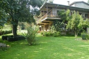 A two-story house with a balcony, surrounded by a well-maintained garden and trees. - Allotjaments Colomer-Cullell (La Vall d'en Bas)
