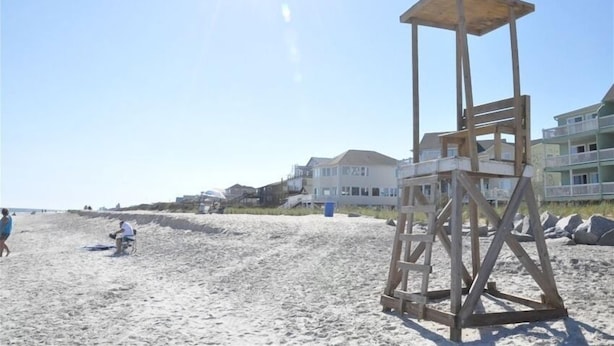 En strand med et livredder-tårn, sand og huse ud til stranden.