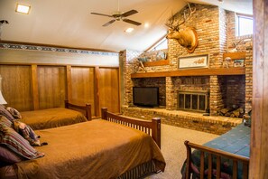 Une chambre avec deux lits, une cheminée et une tête de cerf accrochée au mur.