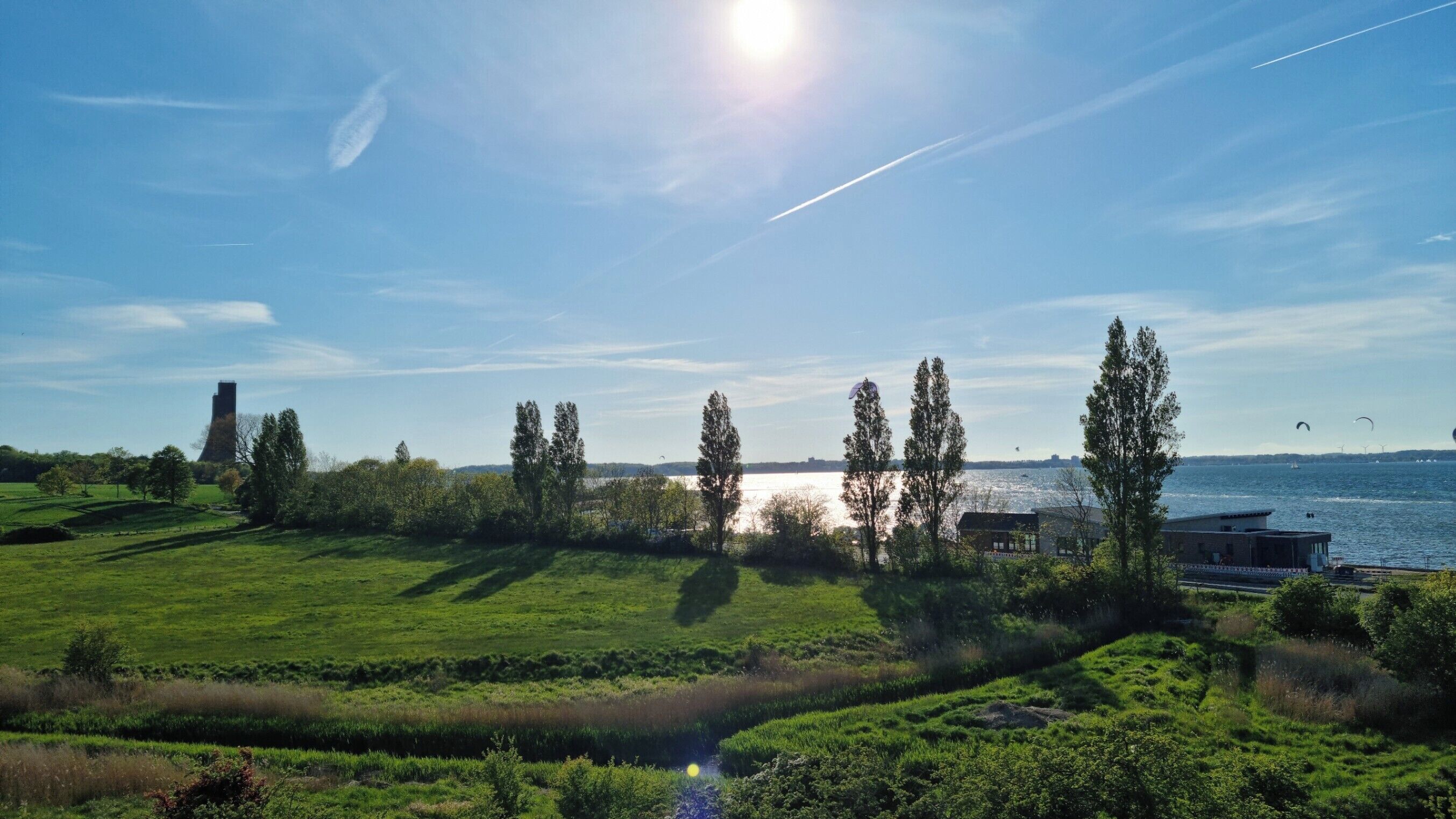 Ett grönskande landskap med en vattenyta, träd och en byggnad i fjärran.