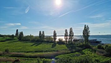 Ett grönskande landskap med en vattenyta, träd och en byggnad i fjärran.