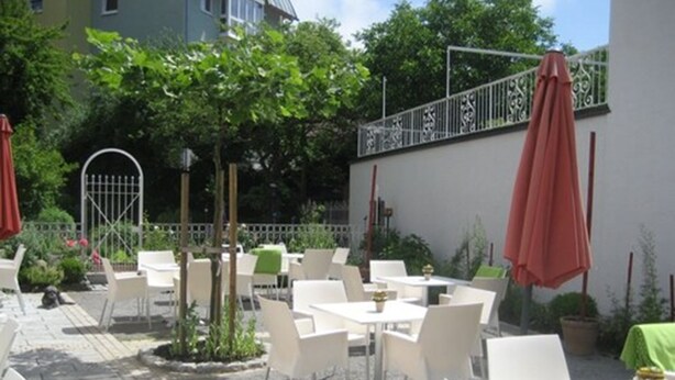 An outdoor patio area with white tables and chairs, surrounded by greenery and a metal fence. - Hotel Gasthof Goldener Adler (Horb am Neckar)