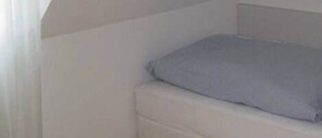 A small, white, single-bed room with a sloped ceiling and wooden flooring.