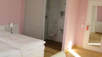Un dormitorio con cama, una silla y un baño visible a través de una puerta abierta.