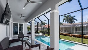 A modern indoor pool area with glass walls, wicker furniture, and a ceiling fan. - 4 Bedroom, 4 Bathroom Custom Home with pool! 5 Min Walk to Beach! (Marco Island)