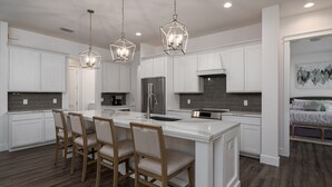 A modern kitchen with white cabinetry, a central island with bar stools, stainless steel appliances, and geometric pendant lighting. - 4 Bedroom, 4 Bathroom Custom Home with pool! 5 Min Walk to Beach! (Marco Island)