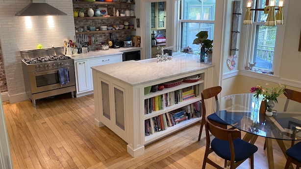 Une cuisine moderne dotée d’un îlot central, d’un plancher en bois et d’un coin repas avec une table et des chaises en verre.