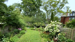 Un jardin où l’on trouve une grande variété de plantes et de fleurs, une clôture en bois et un sentier recouvert d’herbe.