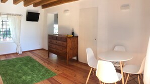 Une pièce avec des poutres en bois, une commode en bois, une table blanche avec des chaises et un tapis vert.
