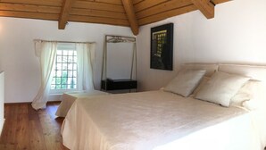 Une chambre avec un plafond en bois, un lit avec une literie blanche, une fenêtre avec des rideaux, un miroir et un tableau accroché au mur.