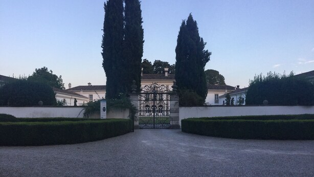 Une entrée imposante, agrémentée d’un portail en fer forgé, de hauts cyprès de chaque côté du portail et d’un beau parterre bien entretenu au premier plan.
