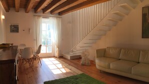 Un salon chaleureux avec un plafond en bois, un escalier, un tapis vert et un canapé beige.