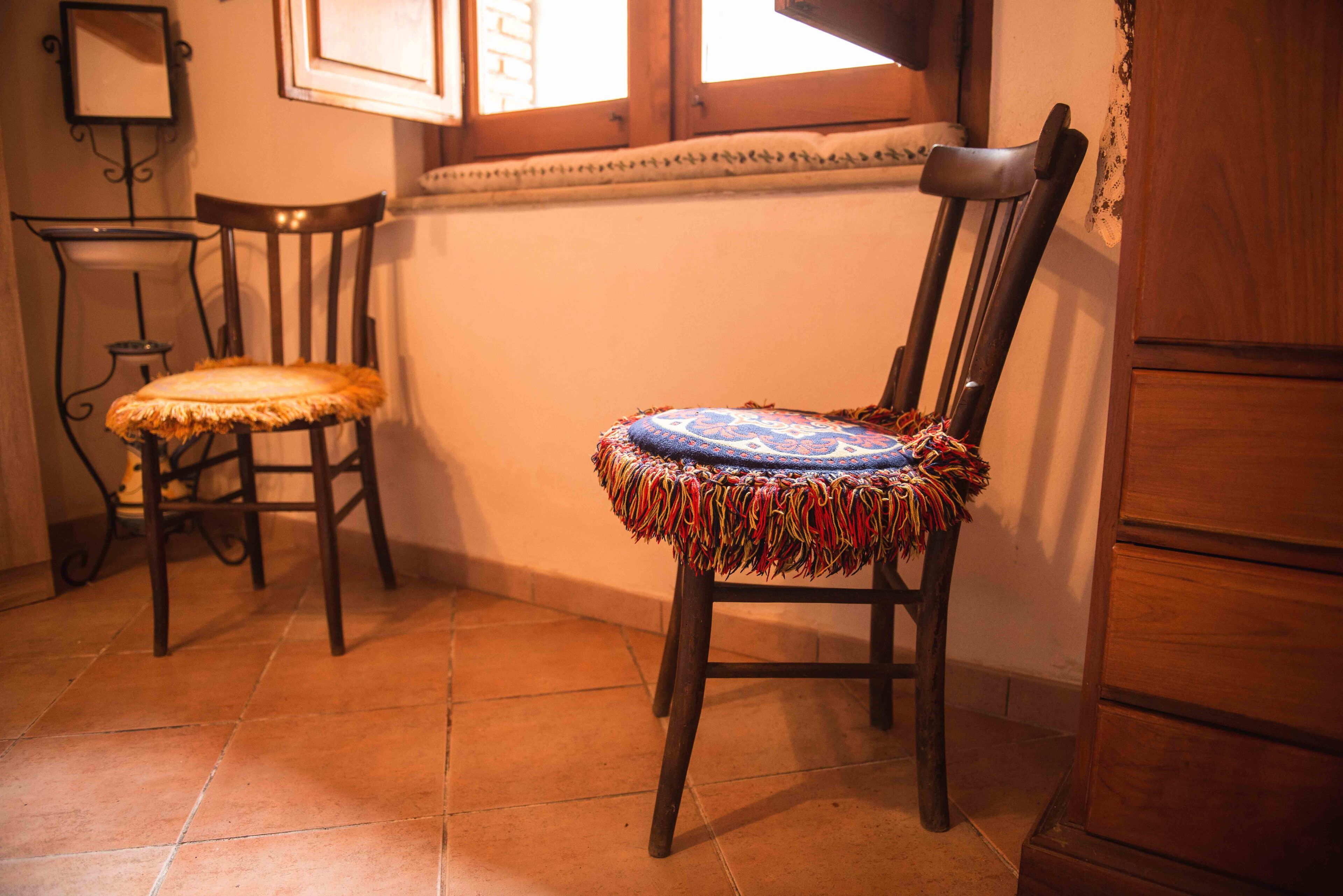 Quarto de canto com duas cadeiras de madeira com assentos acolchoados, uma mesa pequena e um armário.