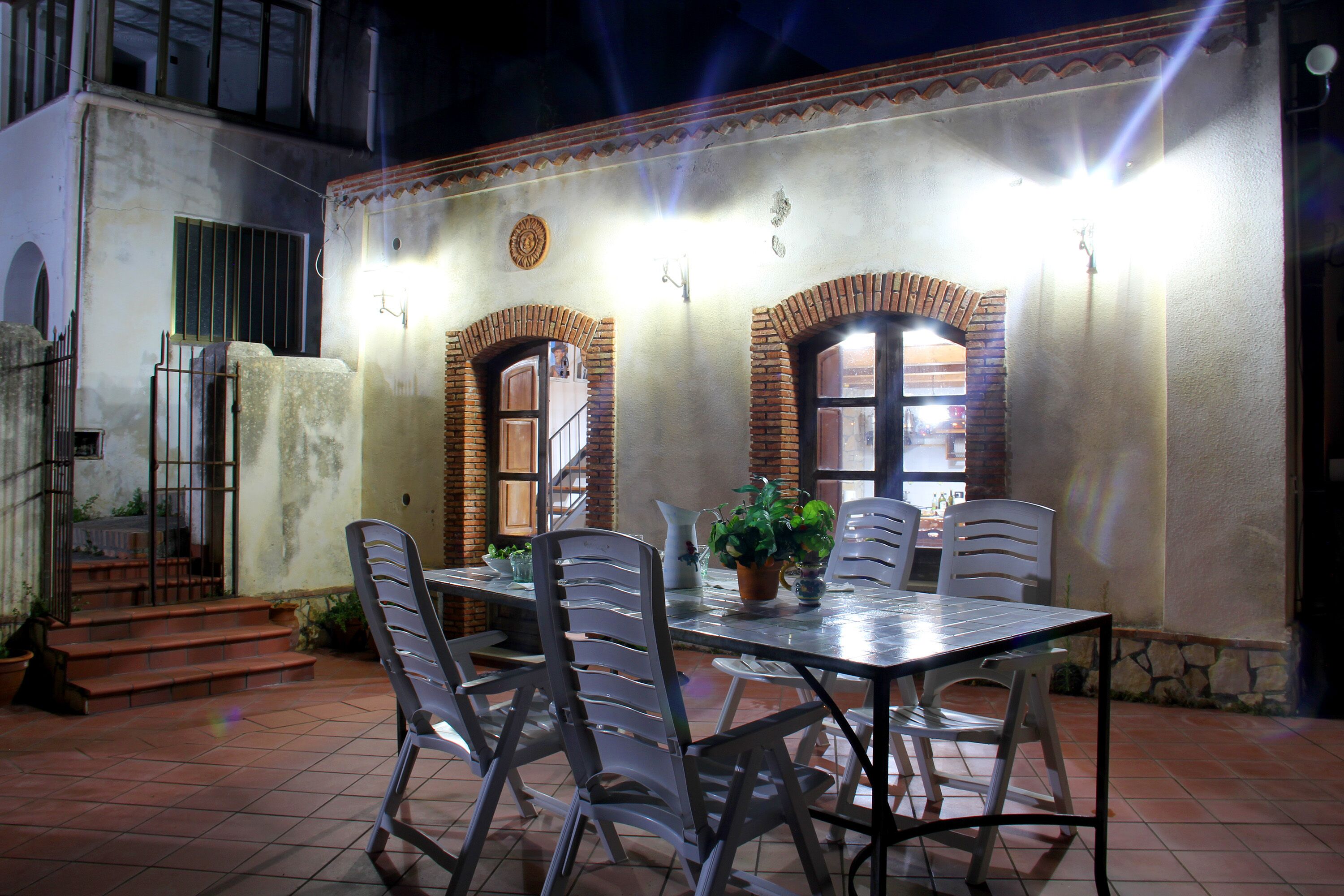 An outdoor patio with a table and chairs, a potted plant, and a staircase leading to an upper level.